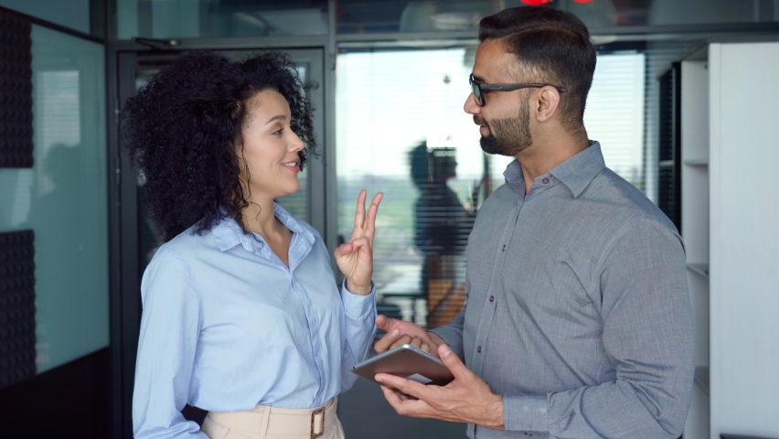 Smiling happy Indian male ceo businessman mentor and female African American manager intern discussing project using tablet device standing in modern corporate office. Business concept. Royalty-Free Stock Footage #1078754879
