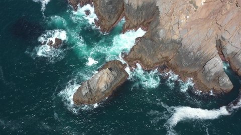 Top view aerial shot of a rocky cliff with waves crashing in the rocks from the Pacific Ocean in Ensenada, Baja California, Mexico.