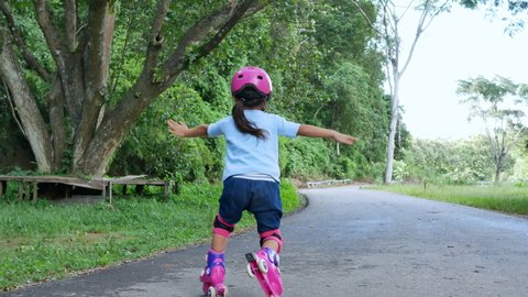 Little girl wearing protection pads and safety helmet learning to roller skate in summer park. Child falls while practicing roller skating on the street. Active outdoor sport for kids.