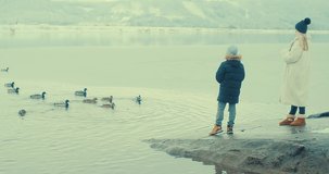Mother and child thrilled by outdoor activities. Family feeding ducks on the lake. Holiday moments, childhood wonder. Winter wonderland. 4K video 