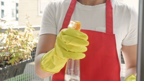 Female hands in yellow gloves cleaning window pane with rag and spray detergent. Washing windows with spray.