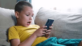 Young boy sitting on the sofa and playing in smartphone. Internet communication, modern technologies and people concept. Video in 4K. 