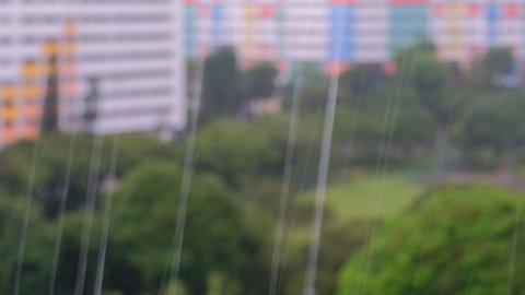 View of heavy falling rain outside window with blur off focus HDB heartland flats and park in the background. Torrential downpour during rainy season in Singapore.