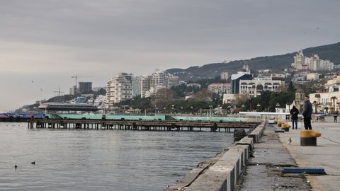 YALTA, RUSSIA-CIRCA2021: Water surface near an embankment against a Yalta cityscape and a mountain by winter day.