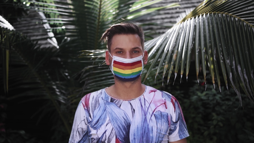 Young gay man wearing a face mask depicting the flag of the LGBT community, a colored rainbow, a young man looking at the camera in support of LGBTQ people
