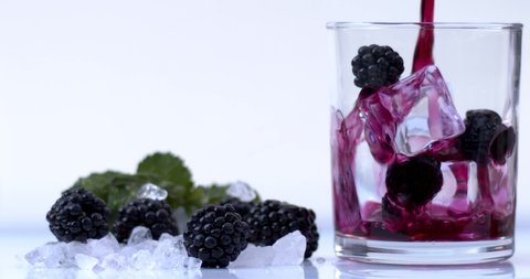 Blackberry juice is poured into a crystal transparent glass on ice with red, natural blackberries on a white background, vitamin and delicious sweet juice. Fimled on cinema camera, 8K downscale. 4K.