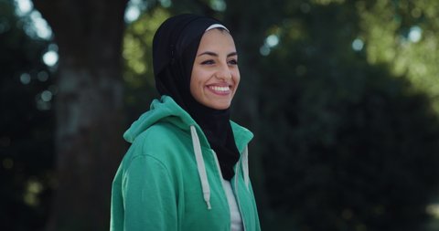 Cinematic close up shot of young happy arab woman wearing burqa is smiling in camera in green city park. 