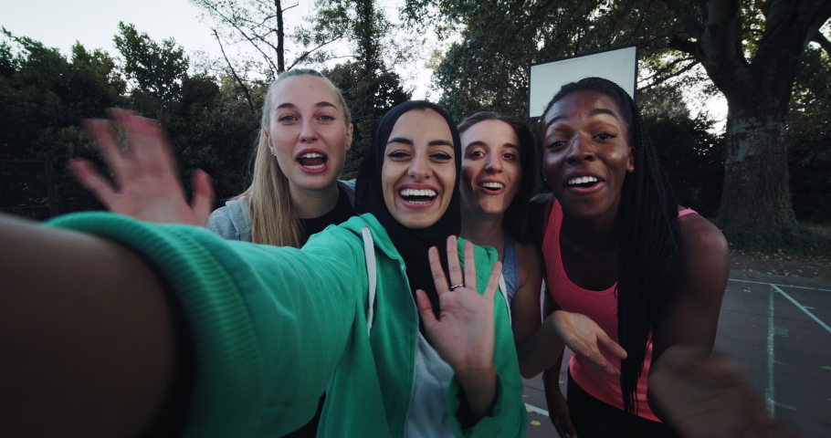 Cinematic shot of young happy girl friends of different ethnicities having fun to make selfie or technology video call on basketball outdoor court after finishing friendly game match.