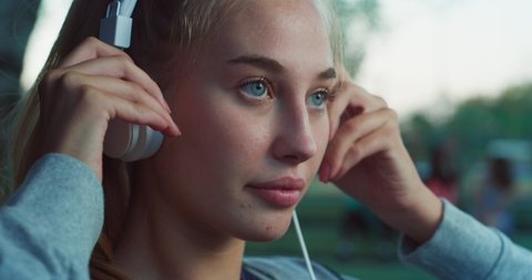 Cinematic close up shot of young blond hair woman is having fun to listening to the music with earphones and dancing on basketball outdoor court after finishing friendly game match at sunset.