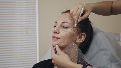 Plastic surgeon drawing correction lines on womans face. Doctor performing nesessary procedure, preparation before upcoming surgery. Concept of beauty, cosmetology.