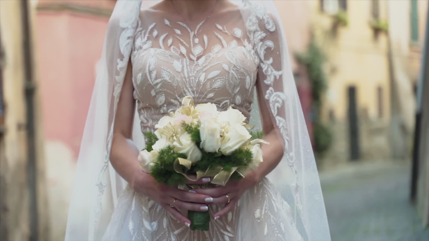 Charming bride in lace wedding dressing posing on the street holding white roses wedding bouquet, bride hands with wedding ring holding flowers bouquet, wedding ceremony flowers in hands of beautiful Royalty-Free Stock Footage #1078796987