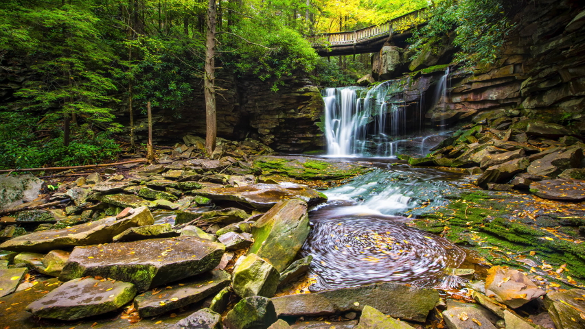 Low angle ground level view timelapse time lapse of Elakala waterfall in Blackwater Falls state park in West Virginia in autumn with colorful leaves foliage over bridge and swirling pool stream