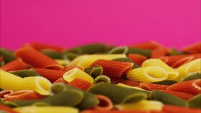 Close-up of rotating colourful macaroni on pink background. Shooting of color pasta in studio. Macro footage of pasta products, spaghetti. Italian food cooking video. 