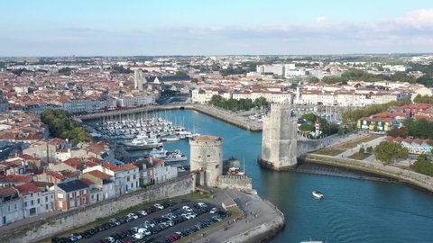 France, La Rochelle, Old Port. A boat passes between the Tour de la Chaine and Saint-Nicolas tower, drone aerial view.