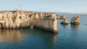 Aerial view of group of people on sup boards paddleboarding in cave of rocks at Ponta de Piedade, Portugal, Lagos, Europe. Women and men practicing sup surfing in Atlantic ocean , 4k footage