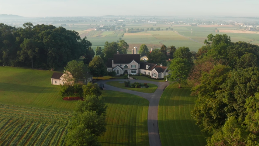 Modern mansion, house, home in rural America. Aerial view of valley and farmland. Dolly forward during misty summer golden hour.