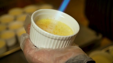 Close-up caramelizing sugar on the top of creme brulee dessert using gas torch. Cane sugar is melted. Classic french dessert.