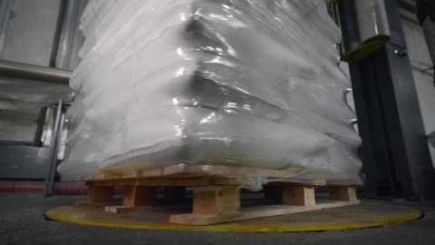 A pallet with bags is packed in foil using a special machine.
