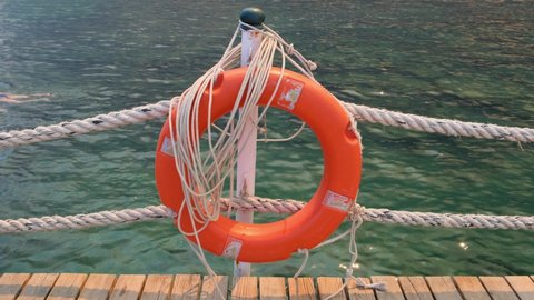 Orange lifeline and sea ropes on the background of the sea and blue sky. Marine ropes and life preserver hanging on a post. Help and safety concept