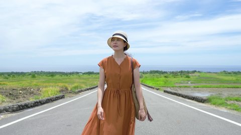 happy asian woman tourist strolling on the road is enjoying the summer sunshine at King Kong Avenue with clear sky and large open farmland in Changbin. taitung.