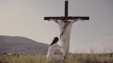 Mary mourns the death of Jesus at his feet. Jesus is crucified on the cross. Wind is blowing. High quality 4k footage