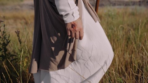Jesus is walking on the grass, touching the ears with his hands. Close-up. There are traces of a crucifixion on the hands. High quality 4k footage