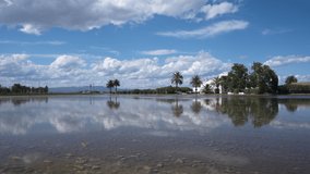 Symmetrical timelapse in a flooded rice field in the ebro delta. View of clouds and typical house with trees reflected in the water.