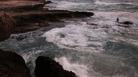 A rocky, wild beach basin, where waves hits the rocks vigorously at twilight. a 4K video clip, Achziv Beach, Israel.