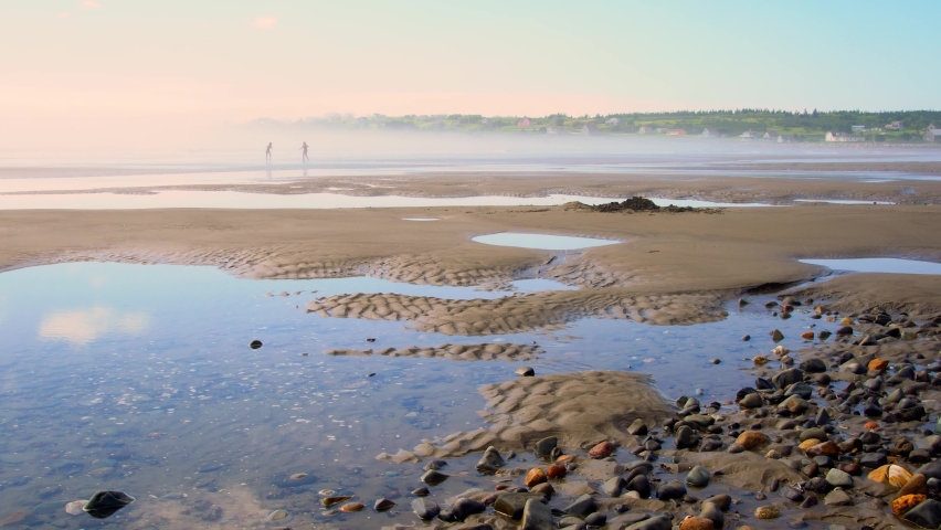 Misty summer morning at the beach.  A tidal pool with people walking in the distance.