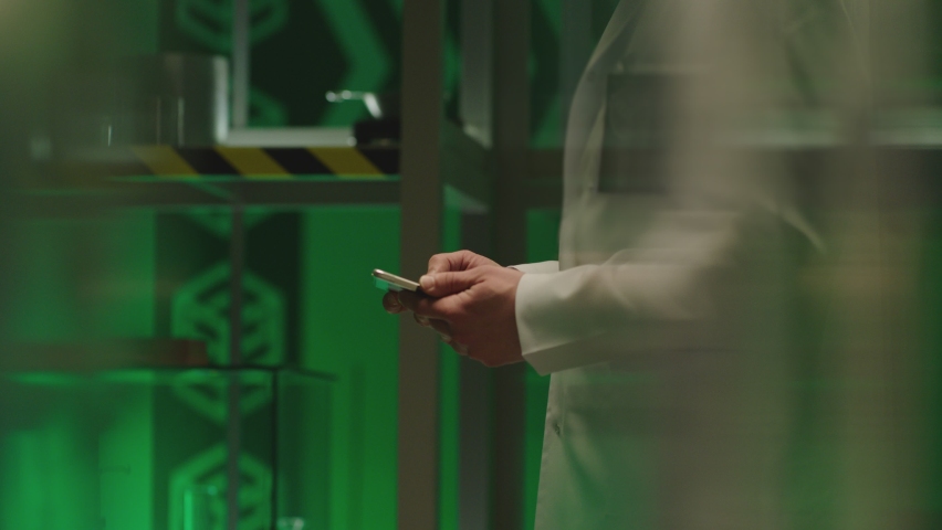 Side unfocused view of male scientist in white uniform holding tablet and working . Man using smart touch screen device in laboratory interior .  Lab equipment in background . Slow motion