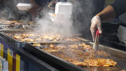 Team of Caribbean ethnicity cooks cooking Jamaican style jerk chicken for customers to take away or takeout at food stall outdoors.