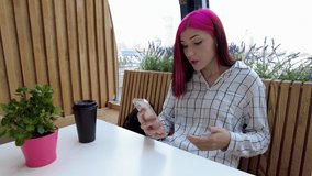 Annoyed red-haired student girl swears with her boyfriend on a smartphone in social networks sitting in cafe.