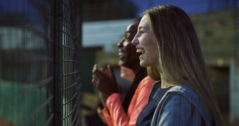Cinematic shot of young excited multiracial teenage female fans are cheering for their team victory on basketball outdoor court during friendly game match.