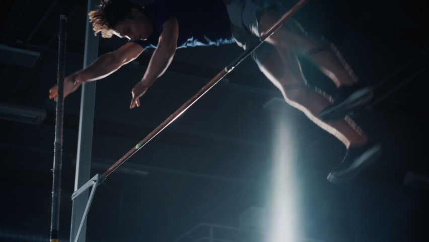 Pole Vault Jumping Championship: Professional Male Athlete Running with Pole Successfully Jumping over Bar and Landing on His Feet. Dramatic Colors, Slow Motion Close-up Shot of Sport Achievement