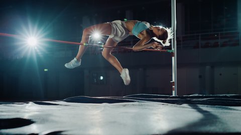 High Jump Championship: Professional Female Athlete Running and Successfully Jumping over Bar. With Determination and Effort Celebrate Winning. Cinematic Light, Dolly Slow Motion Shot