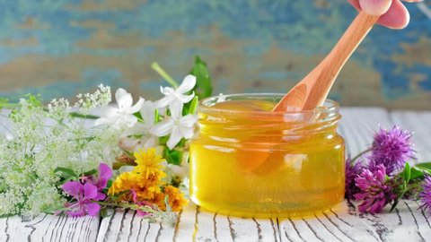 4k. Honey in glass jar with honey dipper over rustic wooden background with Flowers. Healthy organic Thick honey dipping from the wooden honey spoon. Healthy food concept, diet
