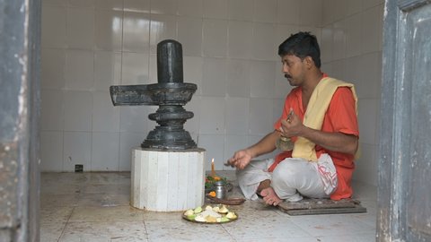 Howrah, West Bengal, India - 26th October 2020 : Hindu priest worshipping lord Shiva by offering water and prayers to Shiv Linga, inside a Shiva Temple. Shiva is most worshipped Hindu God in India.