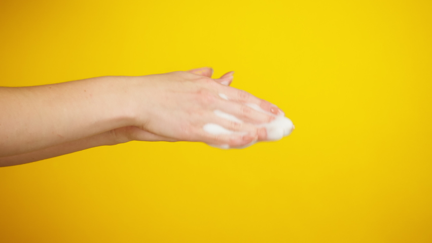 Washing female hands on yellow background, using liquid soap or foam. Prevention of viruses, safety protection. Arms using antibacterial foaming sanitizer close-up. 