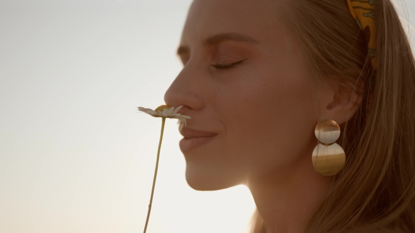 A happy woman is sniffing of chamomile on field at sunset. Carefree girl is enjoying freedom and calmness on rural nature during vacations. Concept of recreation or relax and happiness or summer. Royalty-Free Stock Footage #1078861826