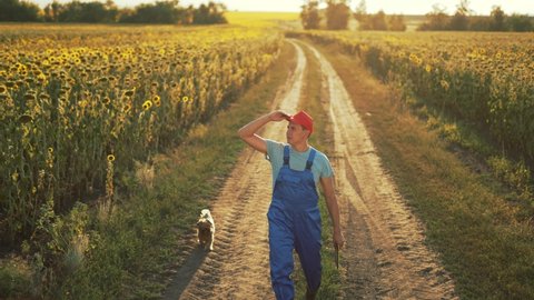 Agriculture. Farmer in rubber boots walks along a rural road. Agricultural business. Farmer in field. Agriculture concept. Farmer walk along rural road in green field. Agricultural business concept
