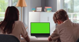 Back view of teen boy and girl sit at desk and study online. Green screen. Schoolchildren watch online lesson on computer sitting at home