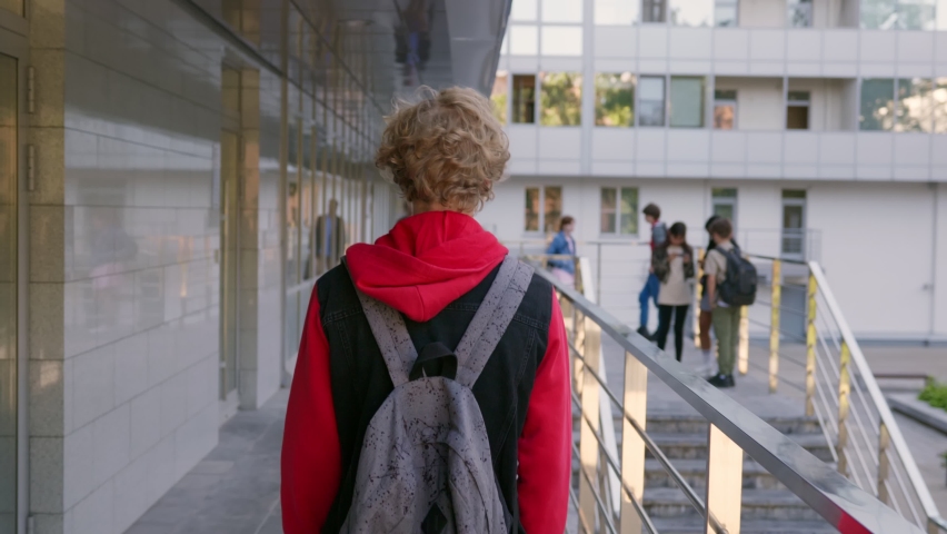 Follow shot of teen schoolboy with backpack walking outdoors. Back view of caucasian male student walk outside school building Royalty-Free Stock Footage #1078864559