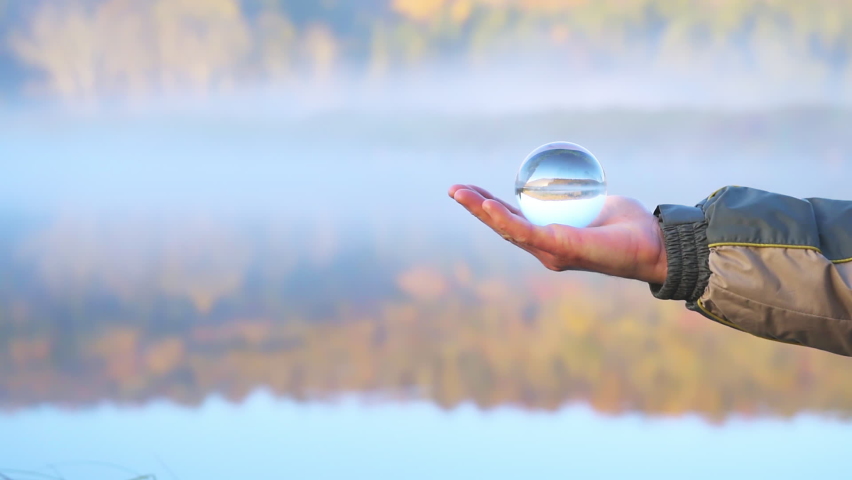 Spruce Knob Lake in West Virginia at sunrise with man hand holding crystal lens ball glass object with bokeh background view of water and forest trees