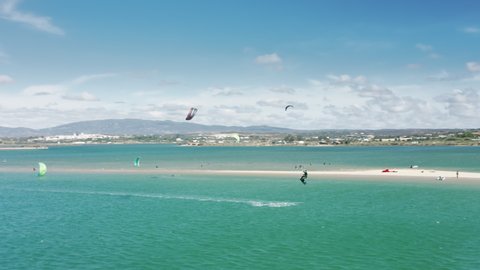 ALVOR, PORTUGAL - 24 JUNE, 2021: Drone shot of sportsmen kiteboarding on beach in summer time, Alvor, Portugal, Europe. Active people training on kiteboards in Atlantic ocean at windy day, 4k footage