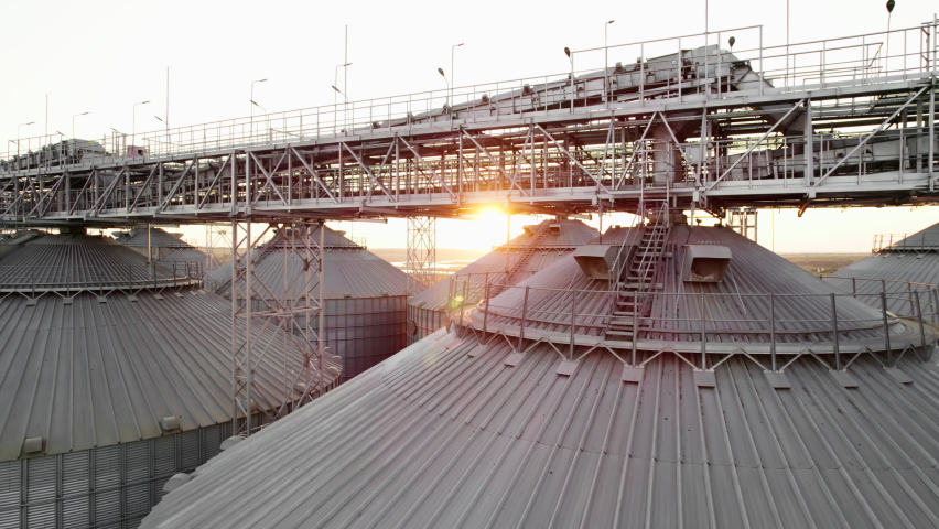 Aerial view Farm Grain Storage Bins wheat field at sunset from top. Steel Granary storage tanks steel warehouse granary for storage of loose grain lens flares on sea port. Industrial