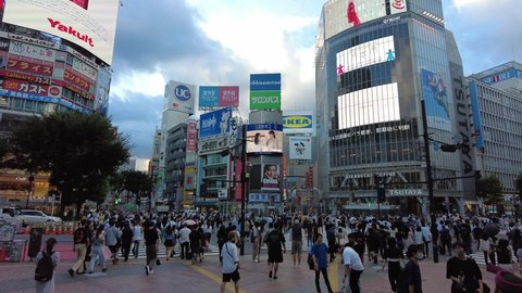 TOKYO, JAPAN - 2021: Shibuya crossing at dusk with lots of people crossing the road