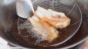 Crispy pork belly fried in hot oil in a pan on the gas stove for breakfast