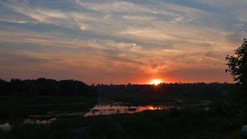 Cloudscape sunset time lapse. Cirrus clouds in sky over Southern Bug river shore with sun reflection in rippled water overgrown by reeds and bulrush plants. Tranquil landscape sundown