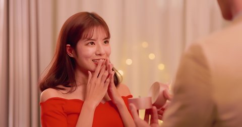 asian man giving propose for marriage to his girlfriend with ring and wear it in living at night home