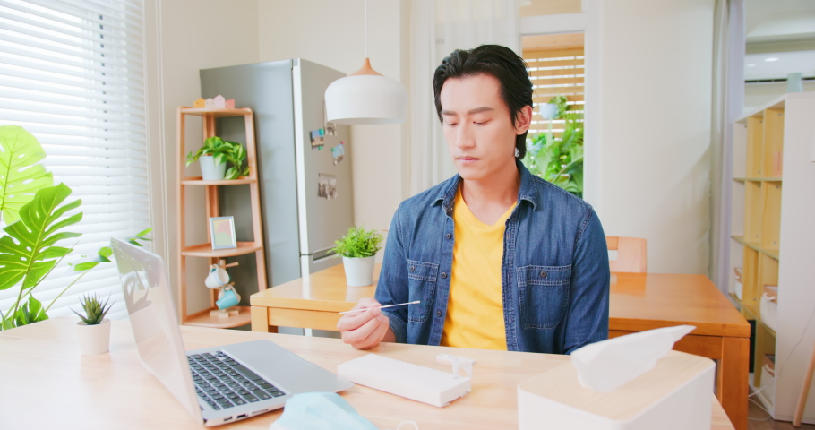 asian man has telemedicine online at home - studying the instructions about COVID-19 self test from laptop with antigen kit on table Royalty-Free Stock Footage #1078886804